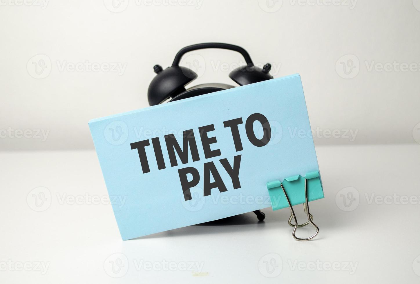 Tempo para pagar é escrito dentro uma azul adesivo perto uma Preto alarme relógio foto