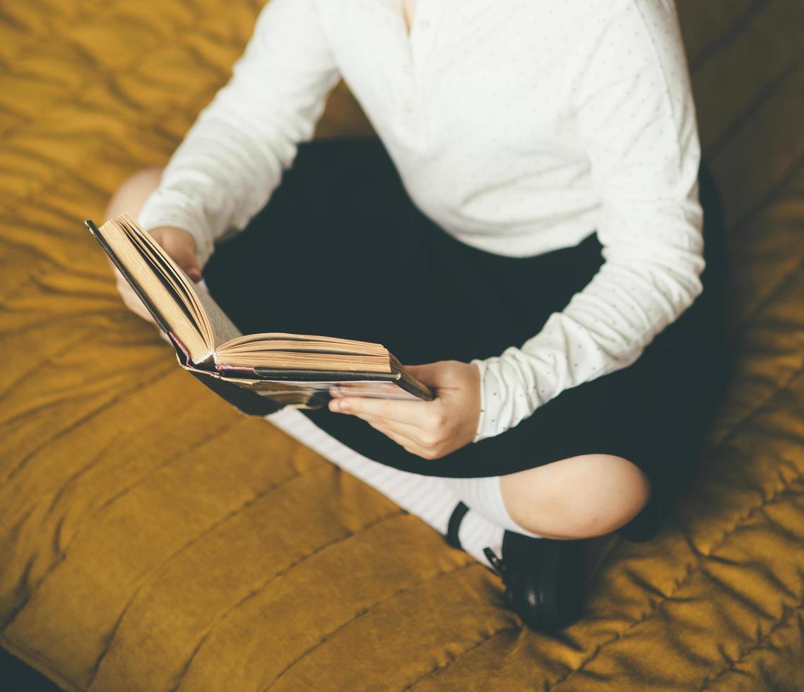 jovem sentada na cama enquanto lê um livro foto