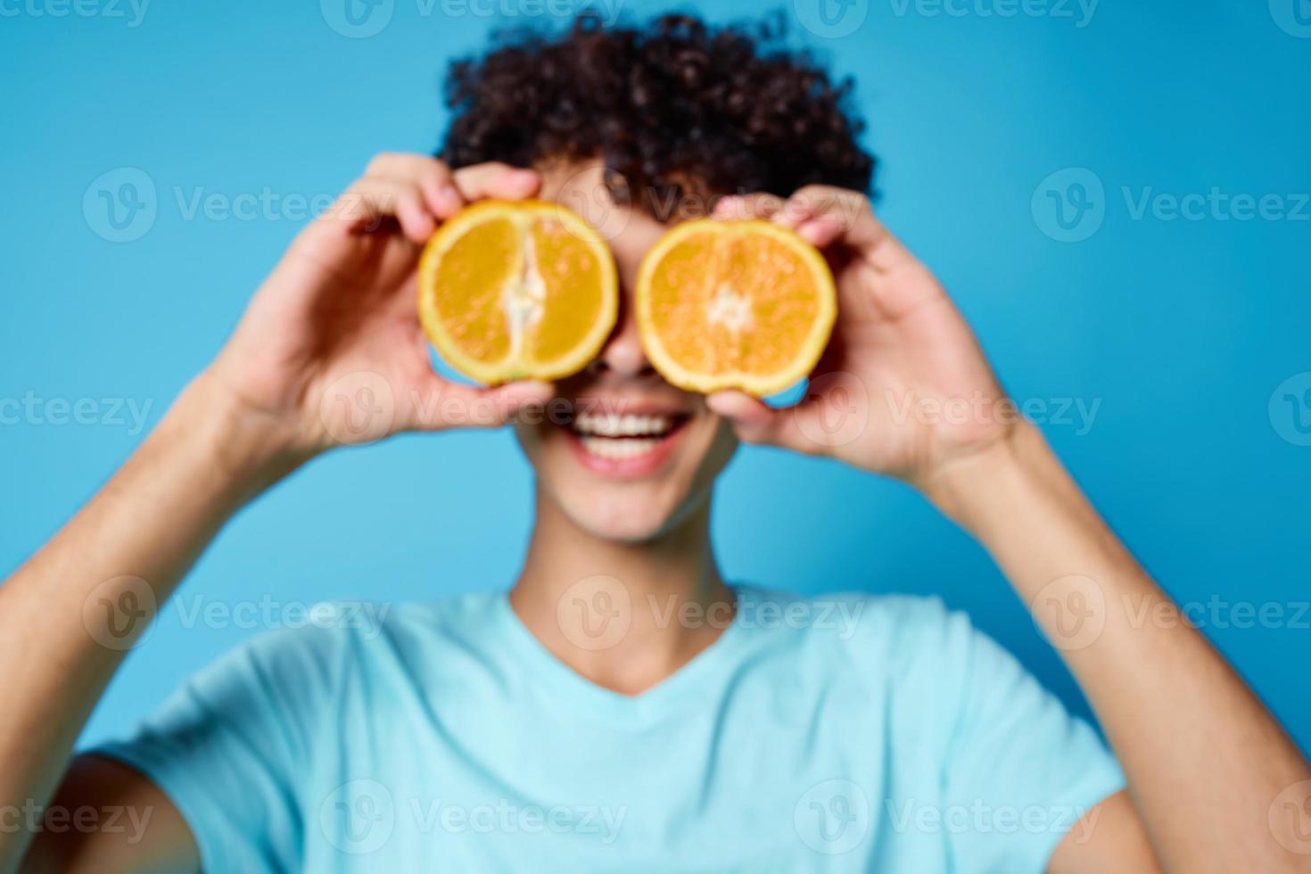 cara com encaracolado cabelo segurando a laranja fruta azul fundo foto