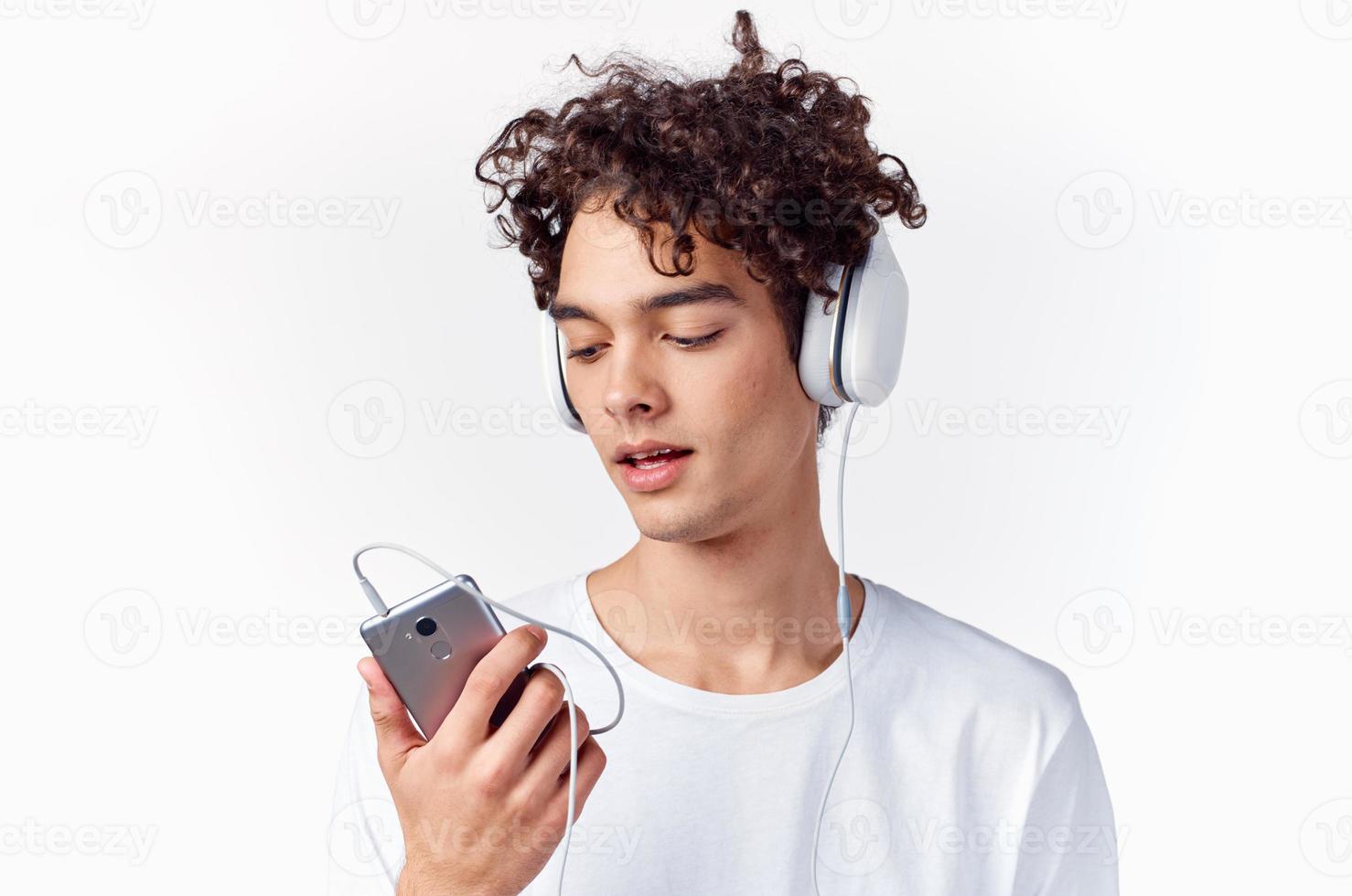 cara com encaracolado cabelo dentro uma branco camiseta escuta para música tecnologia foto