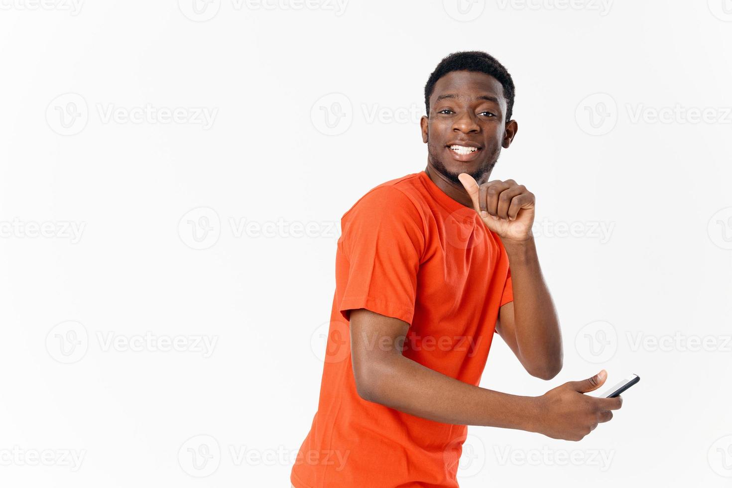 jovem africano americano sorridente e segurando uma tela sensível ao toque telefone dentro dele mão em uma luz fundo foto