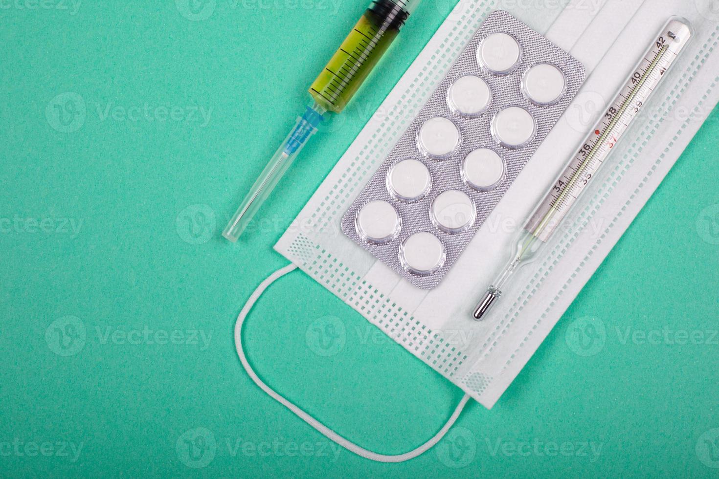 pílulas, seringa, luvas médicas e máscara, meios de proteção contra infecção viral em fundo azul esverdeado foto