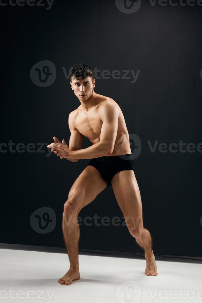 comprimento total desportivo homem com muscular corpo dentro Preto calcinhas posando contra uma Sombrio fundo foto