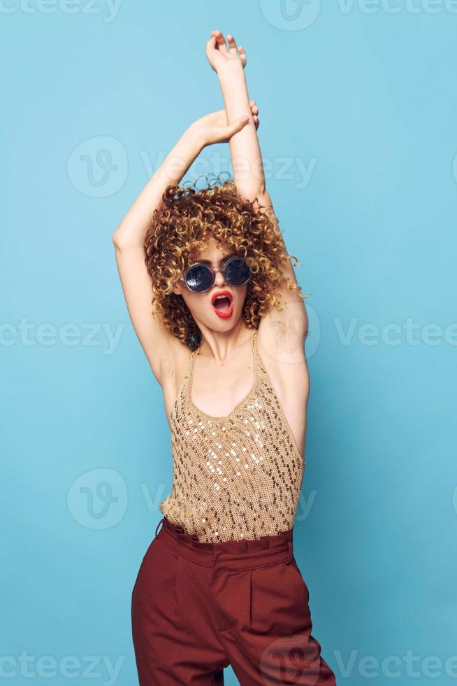 bonita mulher encaracolado cabelo mãos sobre cabeça elegante roupas azul fundo foto