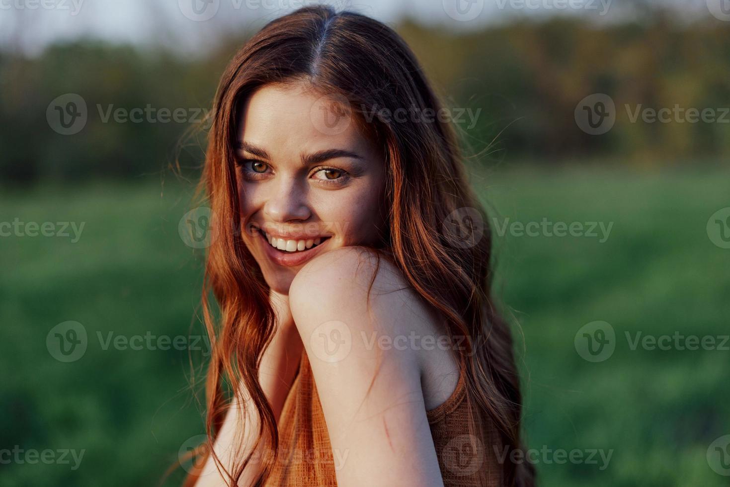 uma jovem mulher rindo e sorridente alegremente dentro natureza dentro a parque com a pôr do sol iluminação iluminador dela grandes vermelho cabelo foto