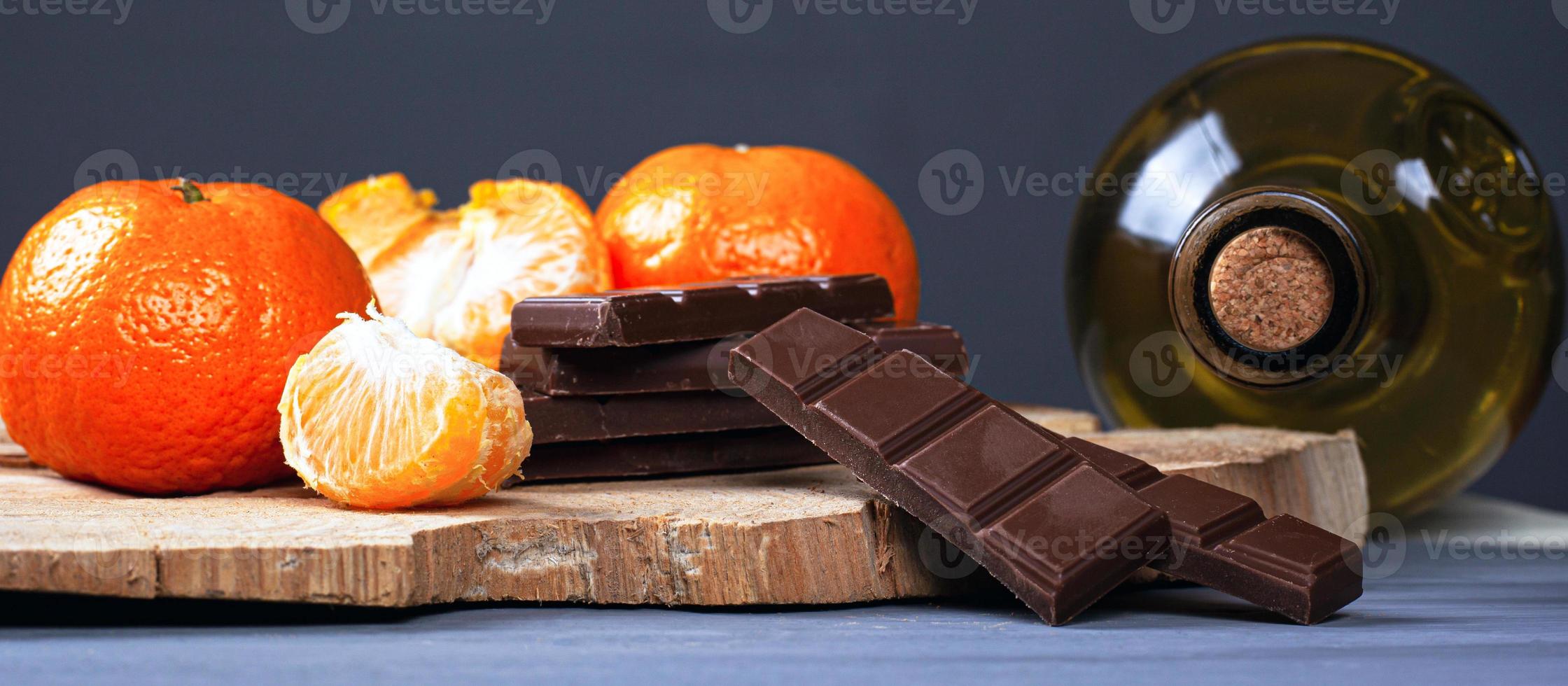 garrafa de vinho branco com fatias de chocolate ao leite e tangerinas em um suporte de madeira foto