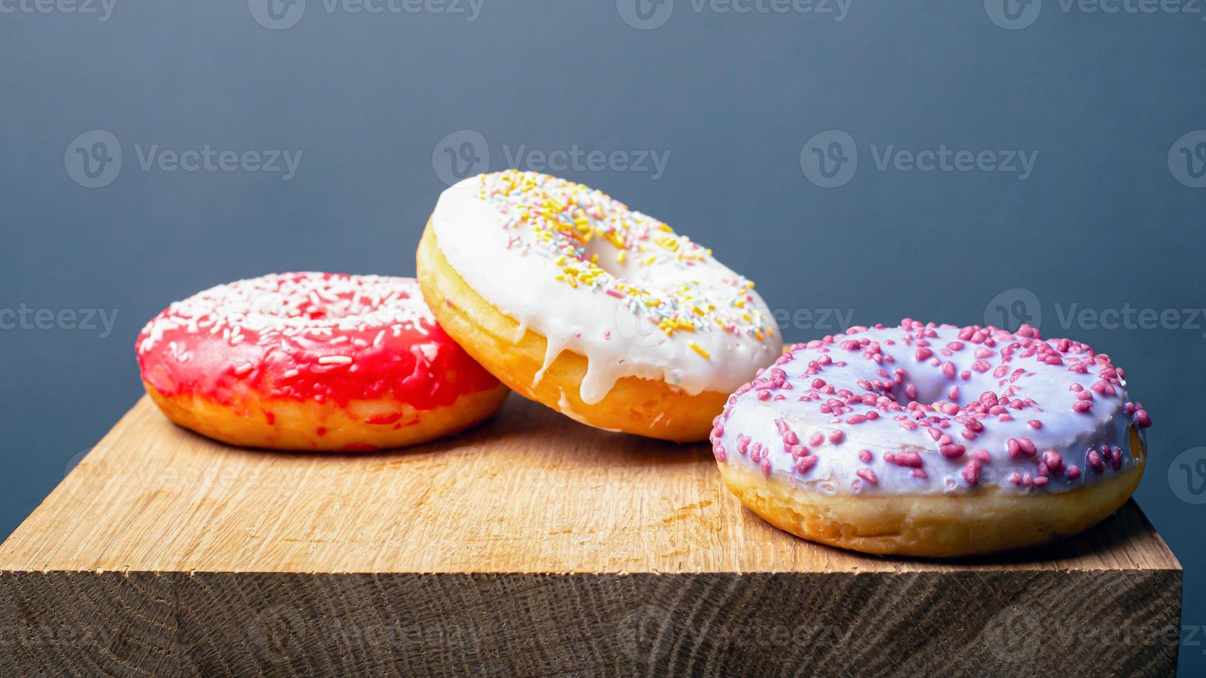 donuts com cobertura multicolorida vermelha, branca e roxa em um suporte de madeira sobre um fundo cinza foto