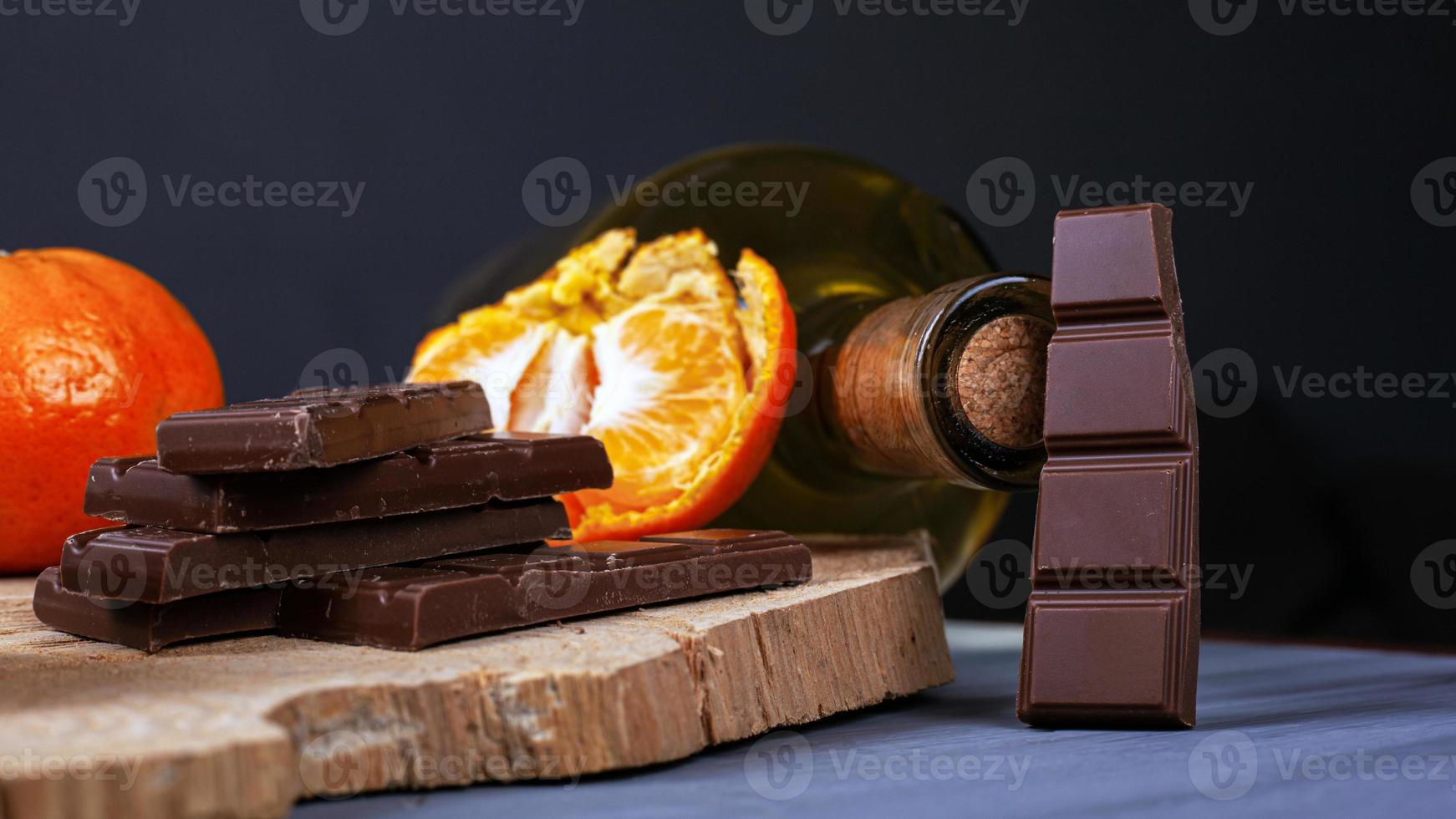 pedaços de chocolate, tangerinas e uma garrafa de vinho em um prato de madeira foto