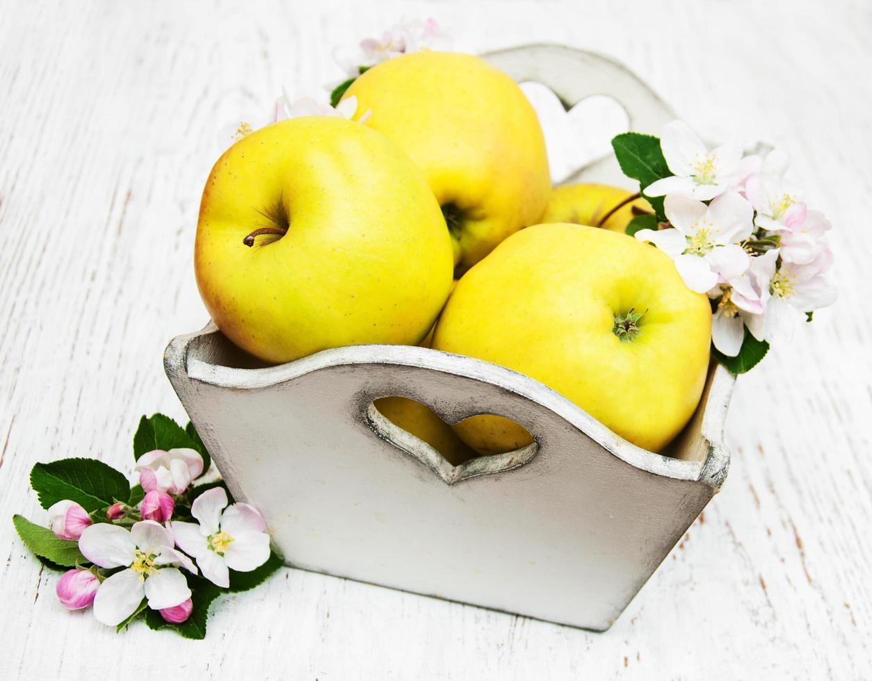 caixa com maçãs e flores de macieira em uma mesa de madeira foto