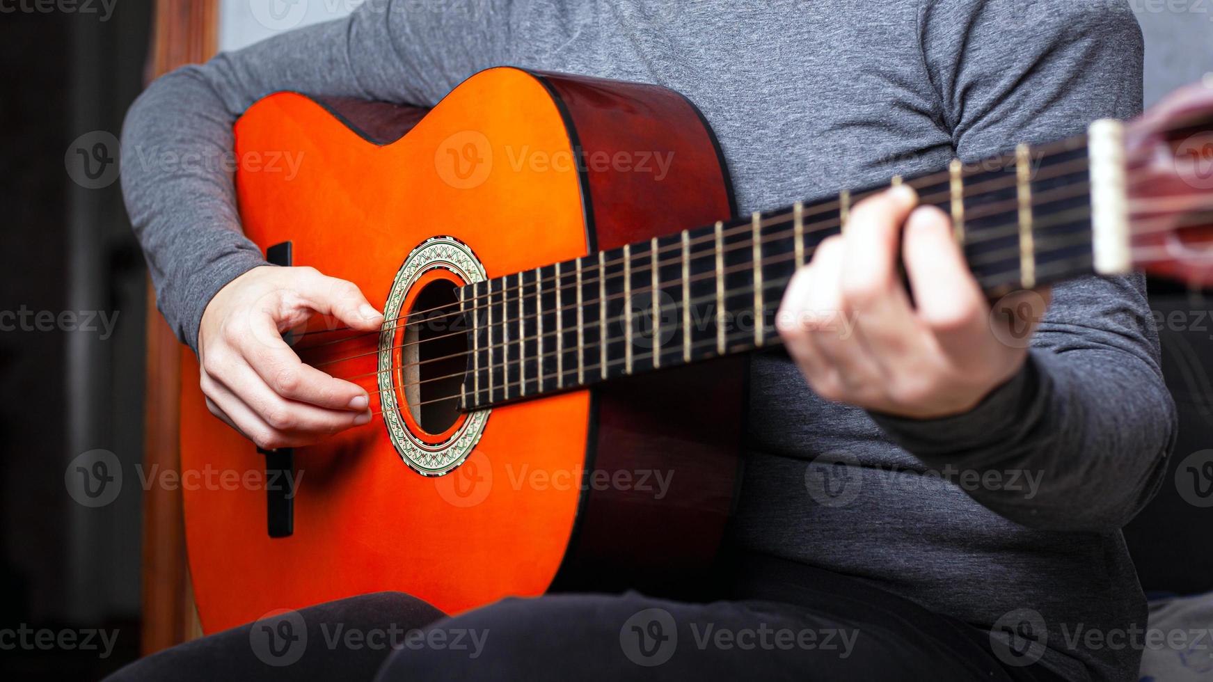 garota tocando um violão laranja segurando o acorde no braço da guitarra foto