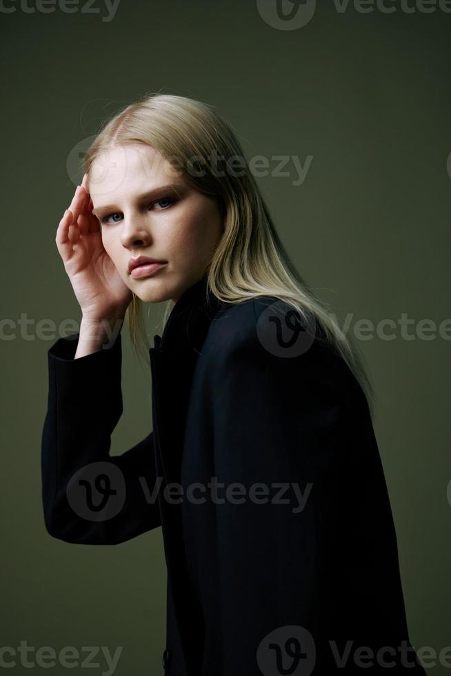 uma fechar retrato do uma Loiras olhando sobre dela ombro dentro uma Preto Jaqueta posando dentro uma estúdio em uma verde fundo. a conceito do à moda moda fotografia foto