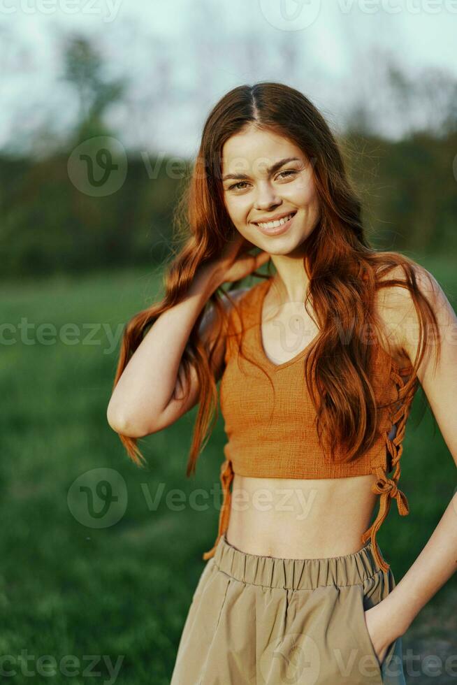 mulher dentro natureza com lindo grandes encaracolado cabelo desfrutando a pôr do sol brilho do sol e sorridente enquanto olhando às a Câmera foto