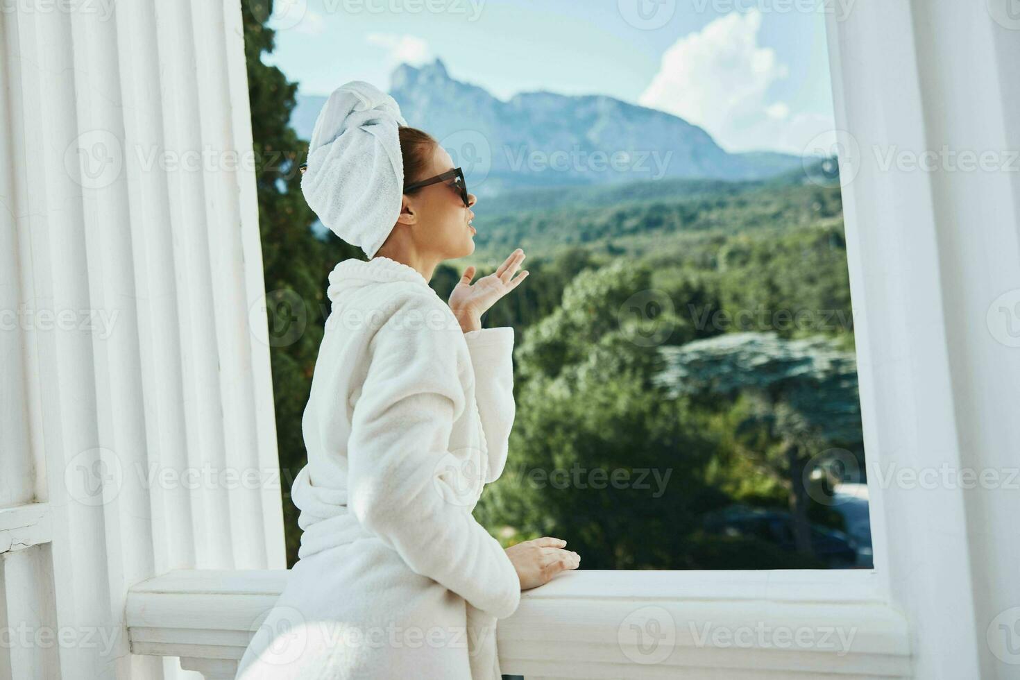 retrato do linda mulher dentro uma branco roupão em a sacada mordeu em verde natureza estilo de vida foto