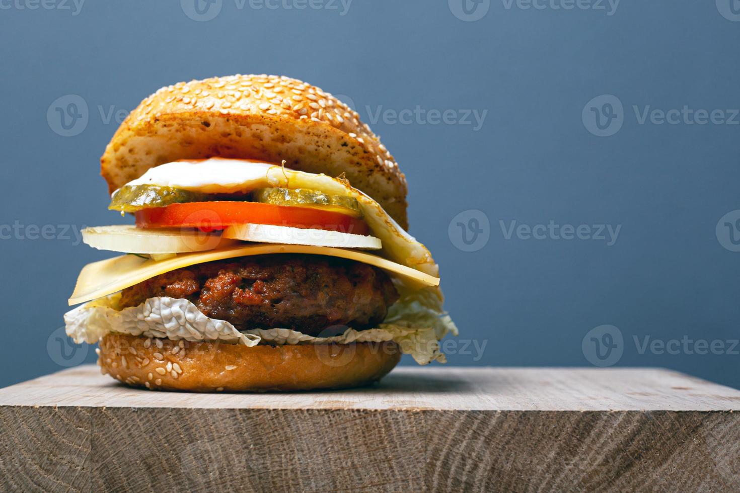hambúrguer suculento com costeleta, queijo e vegetais em um fundo cinza com espaço de cópia foto