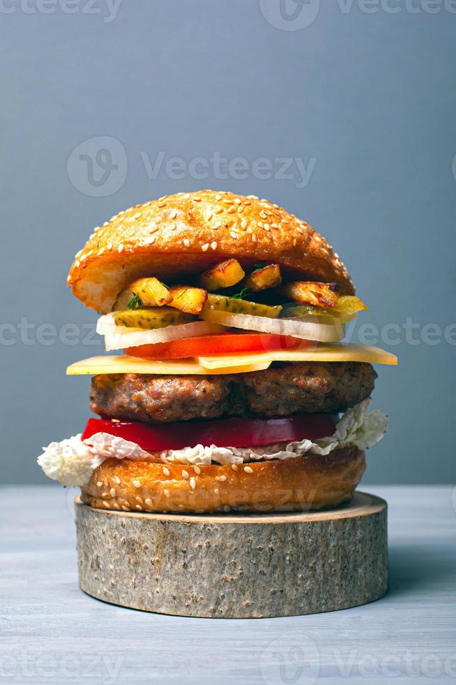 hambúrguer delicioso com uma grande costeleta de carne com legumes, queijo e batatas fritas em um fundo cinza foto