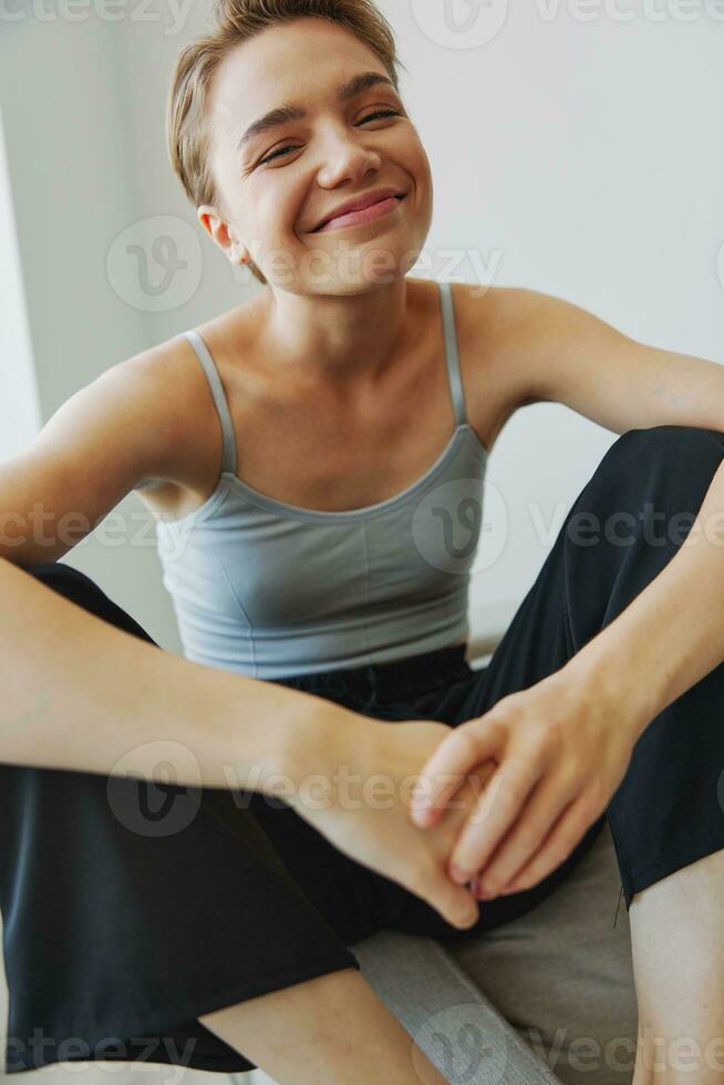 Adolescência menina sentado em a sofá às casa sorridente dentro casa roupas e óculos com uma curto corte de cabelo, estilo de vida sem filtros, livre cópia de espaço foto