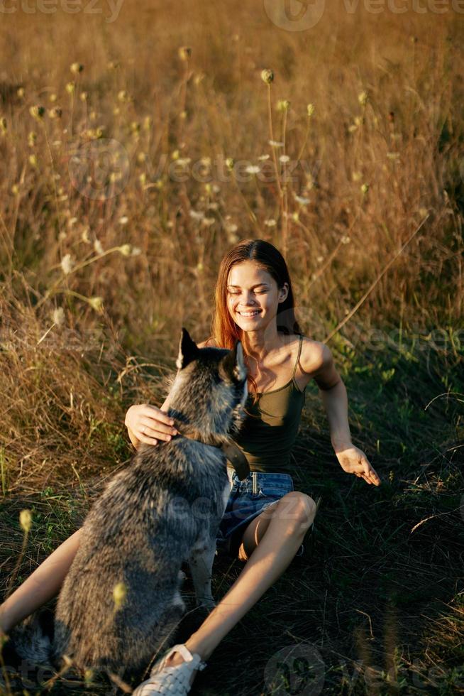 mulher sentado dentro uma campo com uma dachshund cachorro sorridente enquanto gastos Tempo dentro natureza com uma amigo cachorro dentro outono às pôr do sol foto