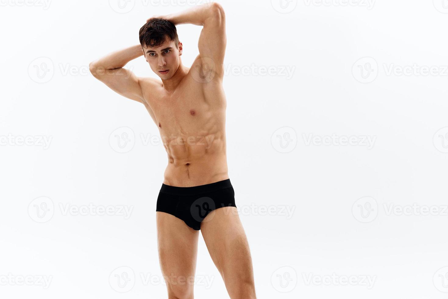atraente homem com nu muscular corpo dentro Sombrio dentro calção cortada Visão dentro luz fundo foto