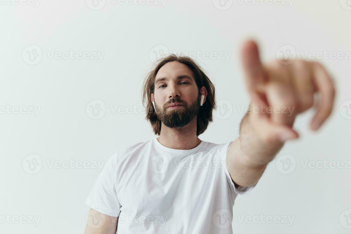 feliz homem ouvindo para música e sorridente dentro uma branco camiseta em uma branco fundo e apontando uma dedo às a tela às a Câmera foto