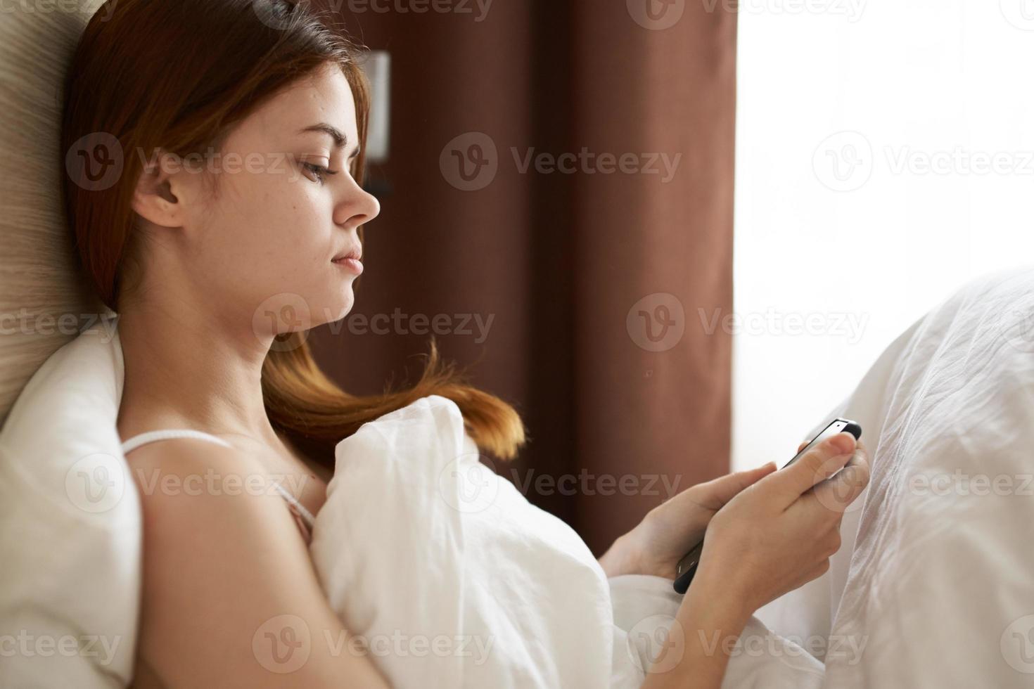 emocional mulher escondeu debaixo cobertor dentro cama perto janela Móvel telefone interior cortinas foto