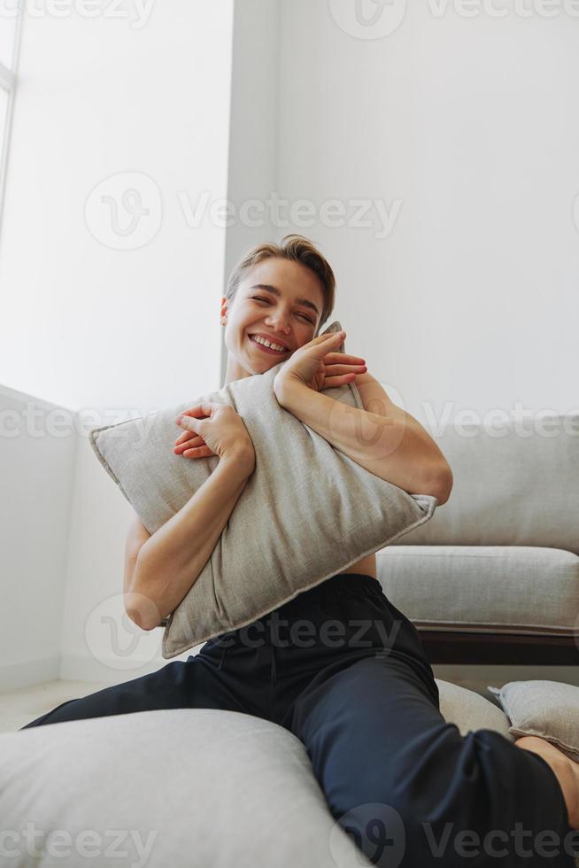Adolescência menina sorrir todos senta às casa perto a sofá e lança acima travesseiros, Diversão jogos e felicidade sem filtros, cópia de Lugar, colocar foto