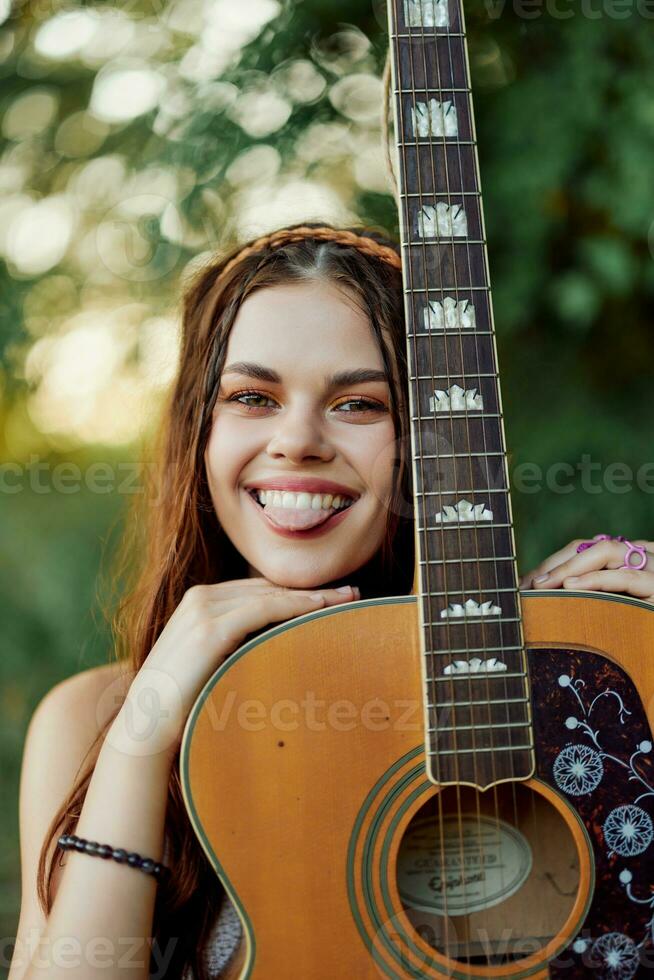 jovem hippie mulher com eco imagem sorridente e olhando para dentro a Câmera com guitarra dentro mão dentro natureza em uma viagem foto