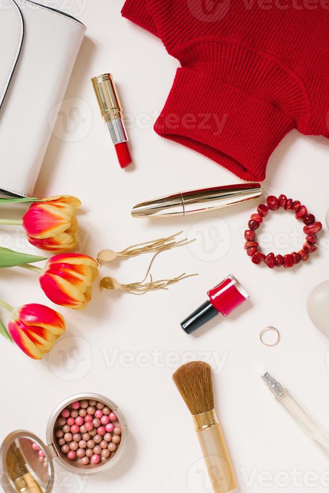 à moda tendendo plano deitar blogueiro para dia dos namorados dia. vermelho suéter, brincos, bolsa, pulseira, anel, batom, sapatos e cosméticos. topo Visão foto