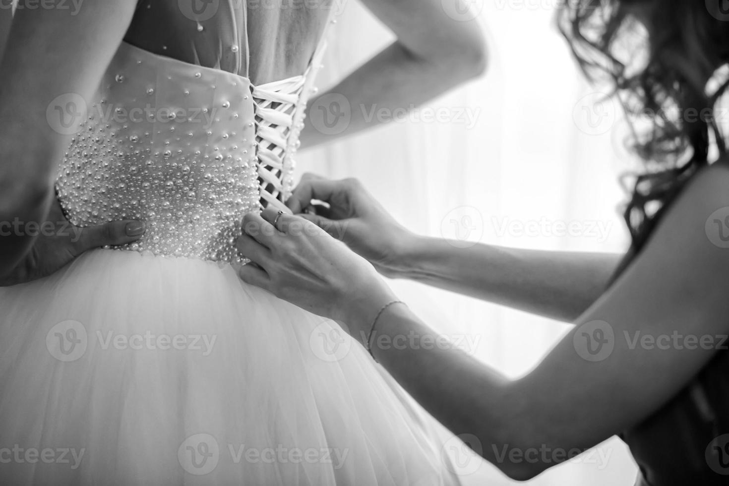 dama de honra ajudando a noiva a fechar um espartilho e a preparar o vestido, preparando a noiva pela manhã para o dia do casamento. encontro de noiva foto