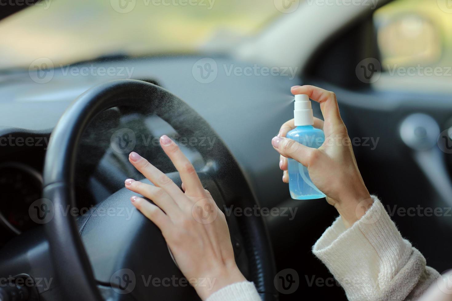 mão de uma mulher borrifando álcool, spray desinfetante no carro, segurança, prevenir a infecção do vírus covid 19, coronavírus, contaminação de germes ou bactérias. desinfetante de álcool, conceito de higiene foto