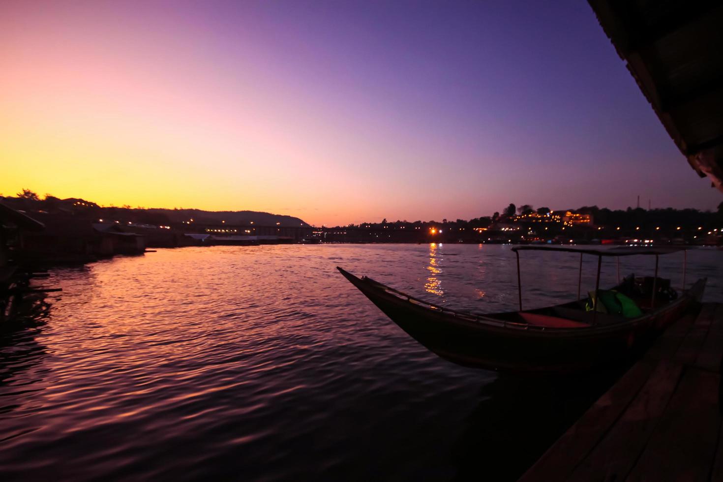 lindo pôr do sol e silhueta do tailandês tradição cauda longa barco dentro a rio perto seg de madeira ponte às sangkhlaburi, Tailândia foto