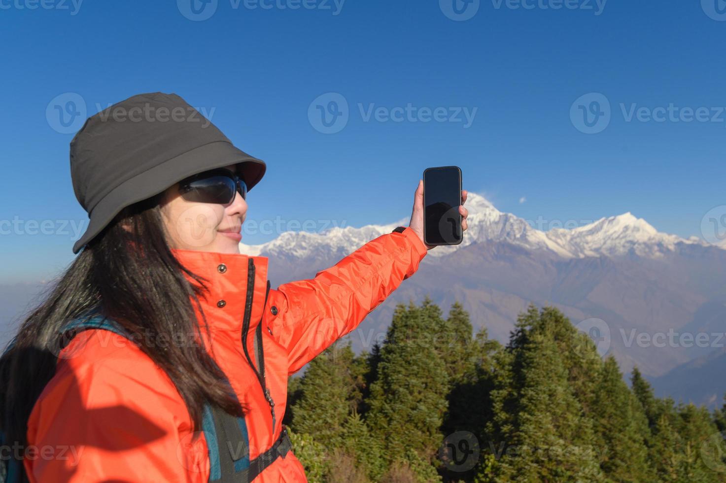 uma jovem viajante leva uma selfie ou uma vídeo ligar enquanto em pé uma topo uma montanha. foto