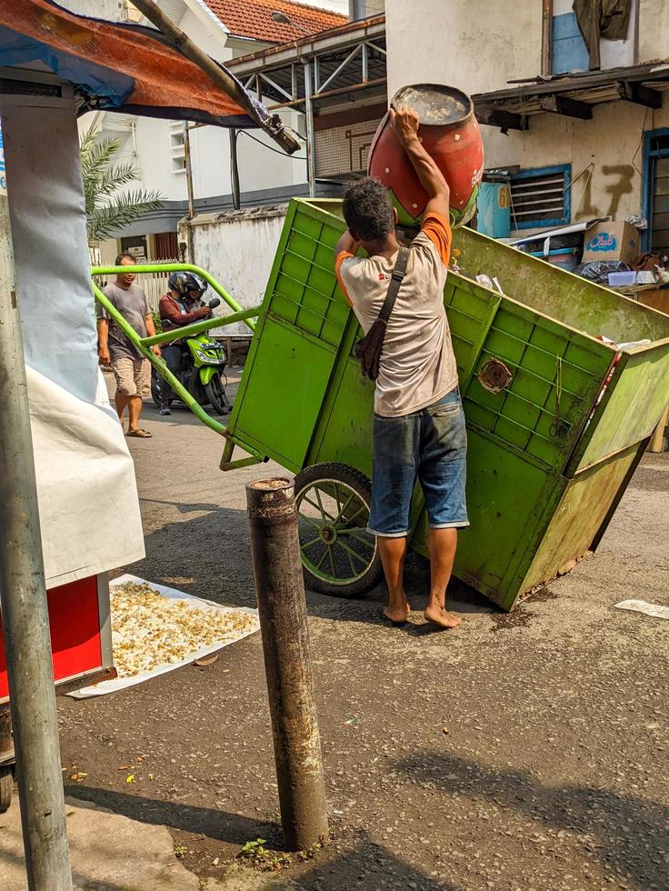 Surabaia, Indonésia - abril, 2023 - uma lixeiro quem lança lixo para dentro a Lixo carrinho foto