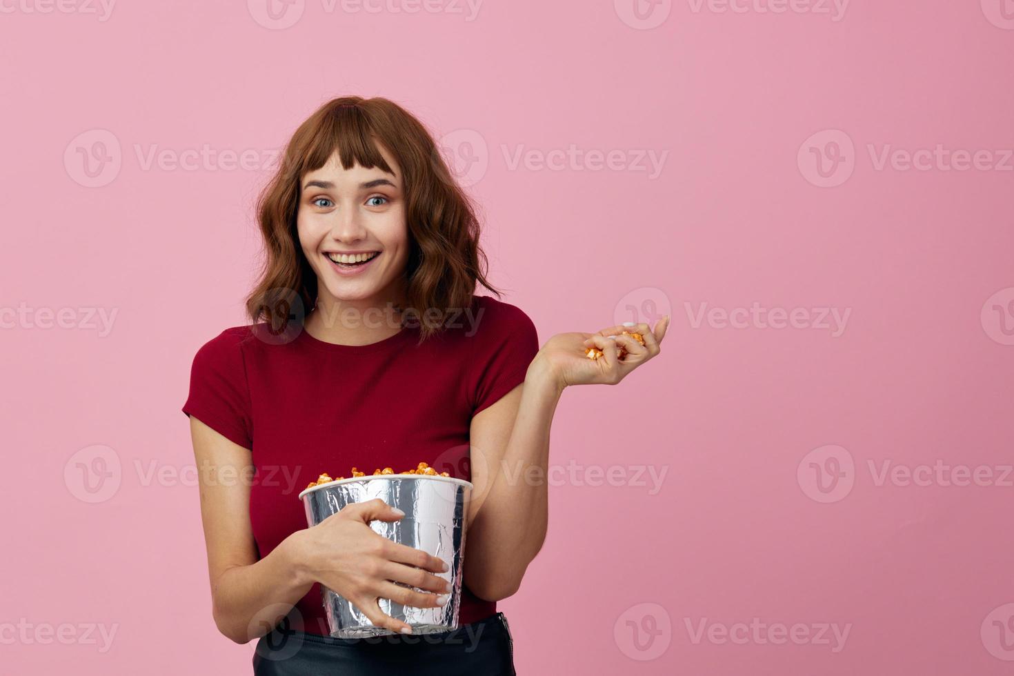 sorridente alegre bonita fofa ruiva senhora dentro vermelho camisa com Pipoca pronto para Assistir filme posando isolado em sobre Rosa estúdio fundo. cópia de espaço bandeira. moda cinema conceito. entretenimento oferta foto