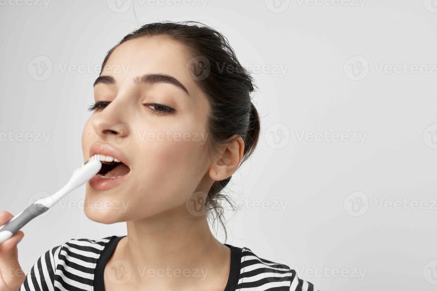 morena dentro uma listrado camiseta escova de dente dentro mão isolado fundo foto