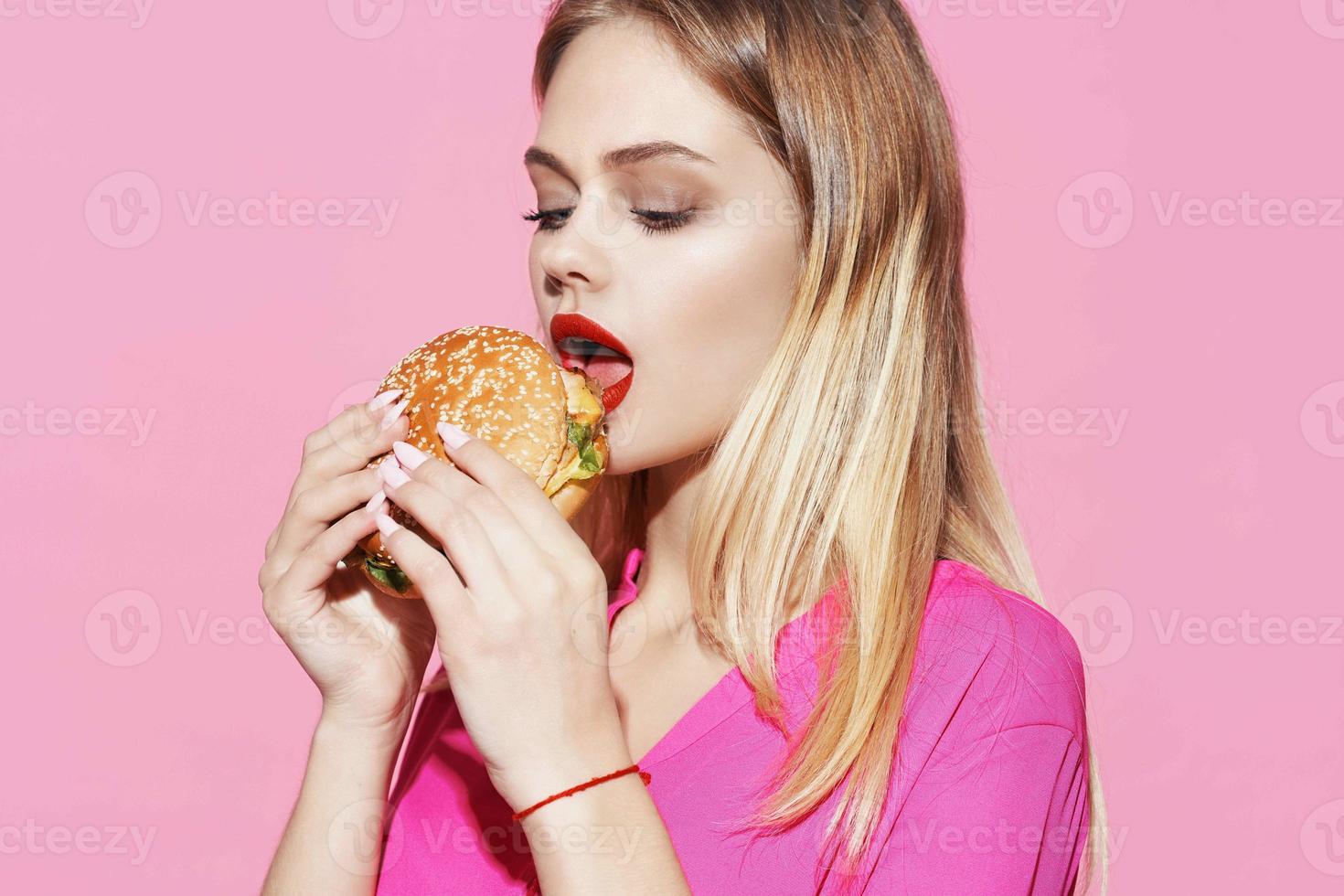 bonita mulher dentro Rosa camisa com Hamburger velozes Comida dieta foto