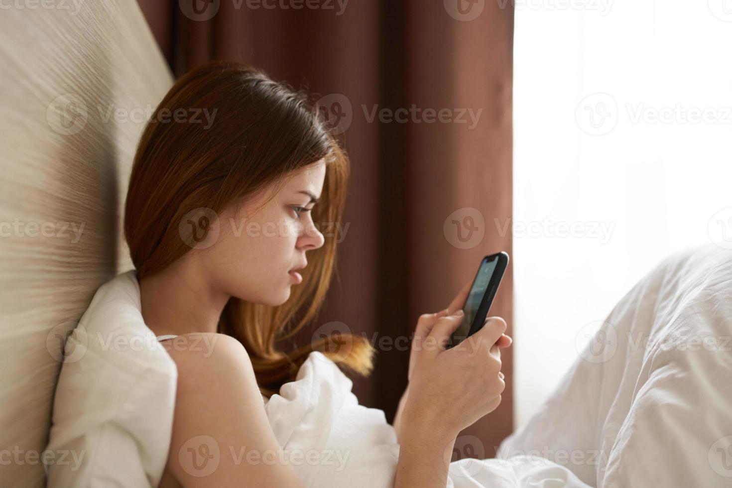 indignado mulher com Móvel telefone dentro cama Projeto interior modelo foto