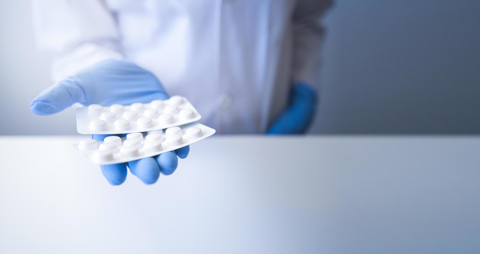 farmacêutico oferecendo embalagem de comprimidos brancos em fundo branco e luvas azuis foto