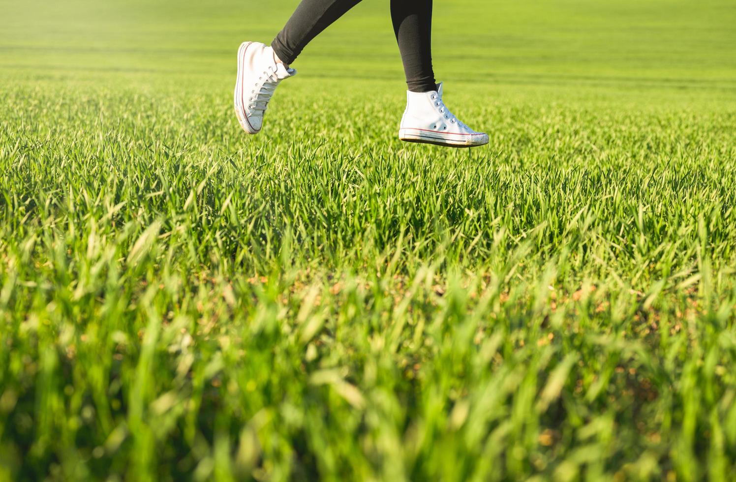 pés de menina com tênis branco pulando em um prado verde foto