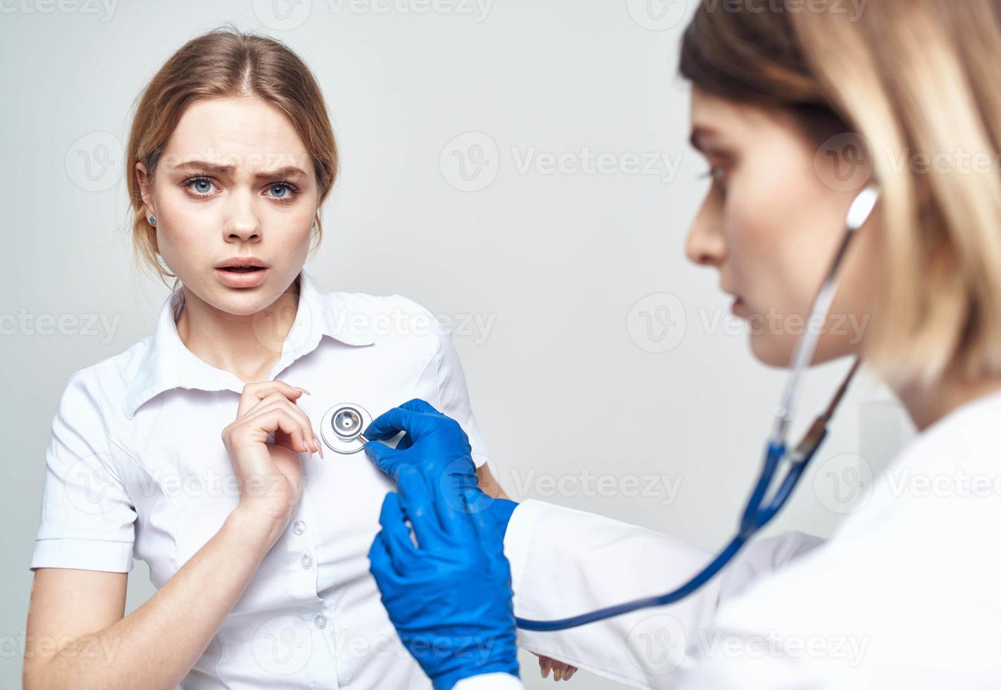 uma paciente senta em uma cadeira e uma mulher médico com uma estetoscópio foto