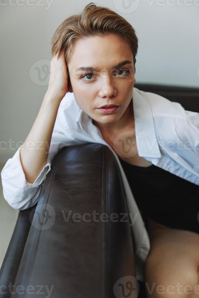 mulheres deitado às casa em a sofá retrato com uma curto corte de cabelo dentro uma branco camisa, sorriso, depressão dentro adolescentes, casa feriado foto