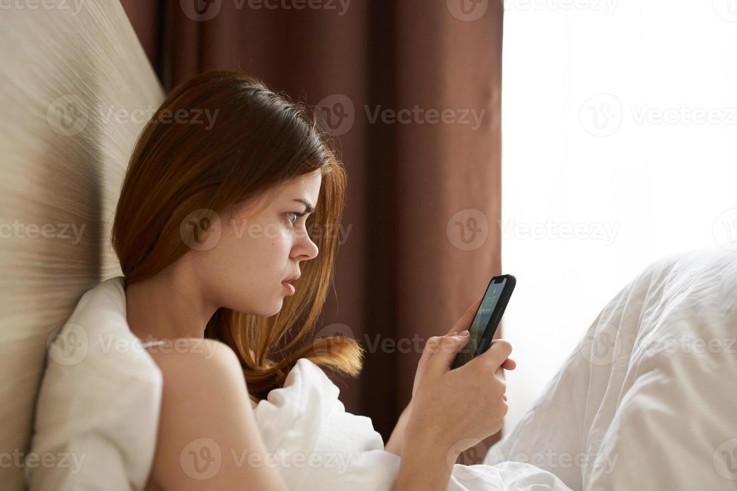indignado mulher com Móvel telefone dentro cama Projeto interior modelo foto