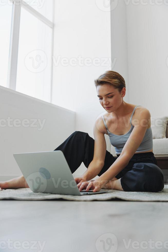 freelance mulher com computador portátil e telefone trabalho a partir de casa sentado em a chão dentro dela casa roupas com uma curto corte de cabelo, livre cópia de espaço foto