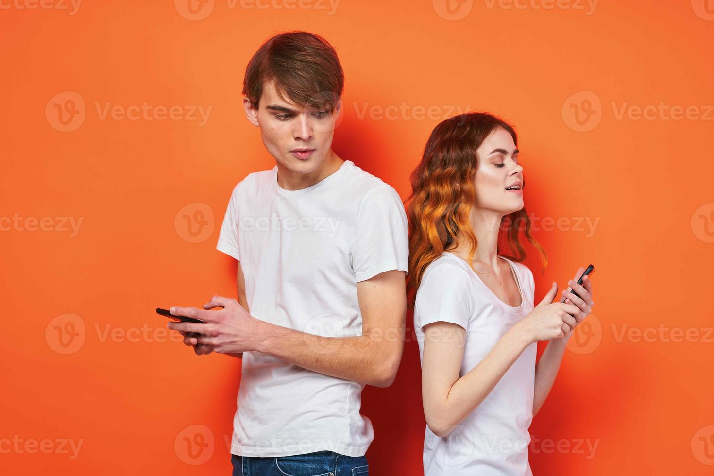 alegre jovem casal dentro branco Camisetas telefones entretenimento tecnologia laranja fundo foto