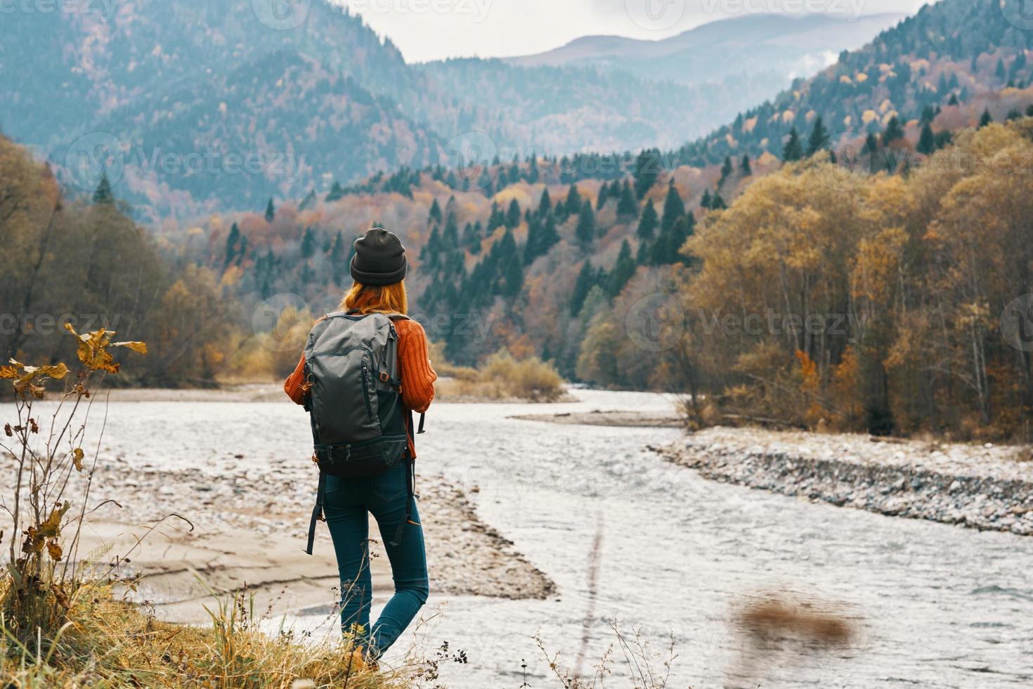 mulher dentro jeans e uma Jaqueta com uma mochila perto a rio dentro a montanhas panorama natureza foto