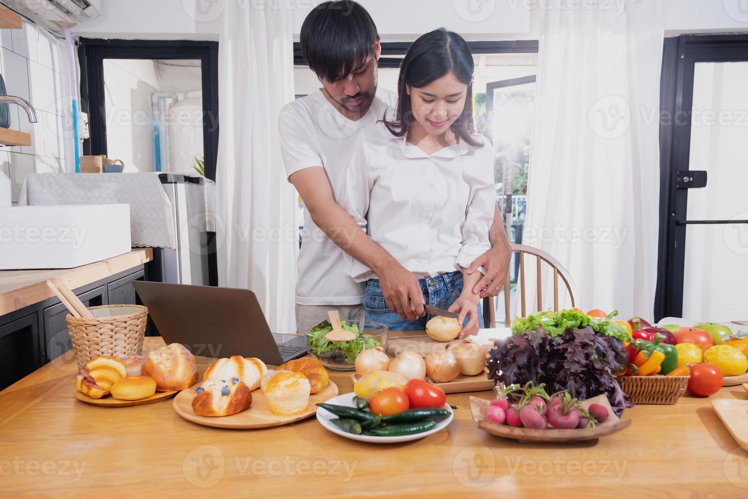 jovem ásia casal cozinhando com frutas e legumes e usando computador portátil dentro a cozinha para cozinhar Comida juntos dentro a família Felizmente, família conceito. foto