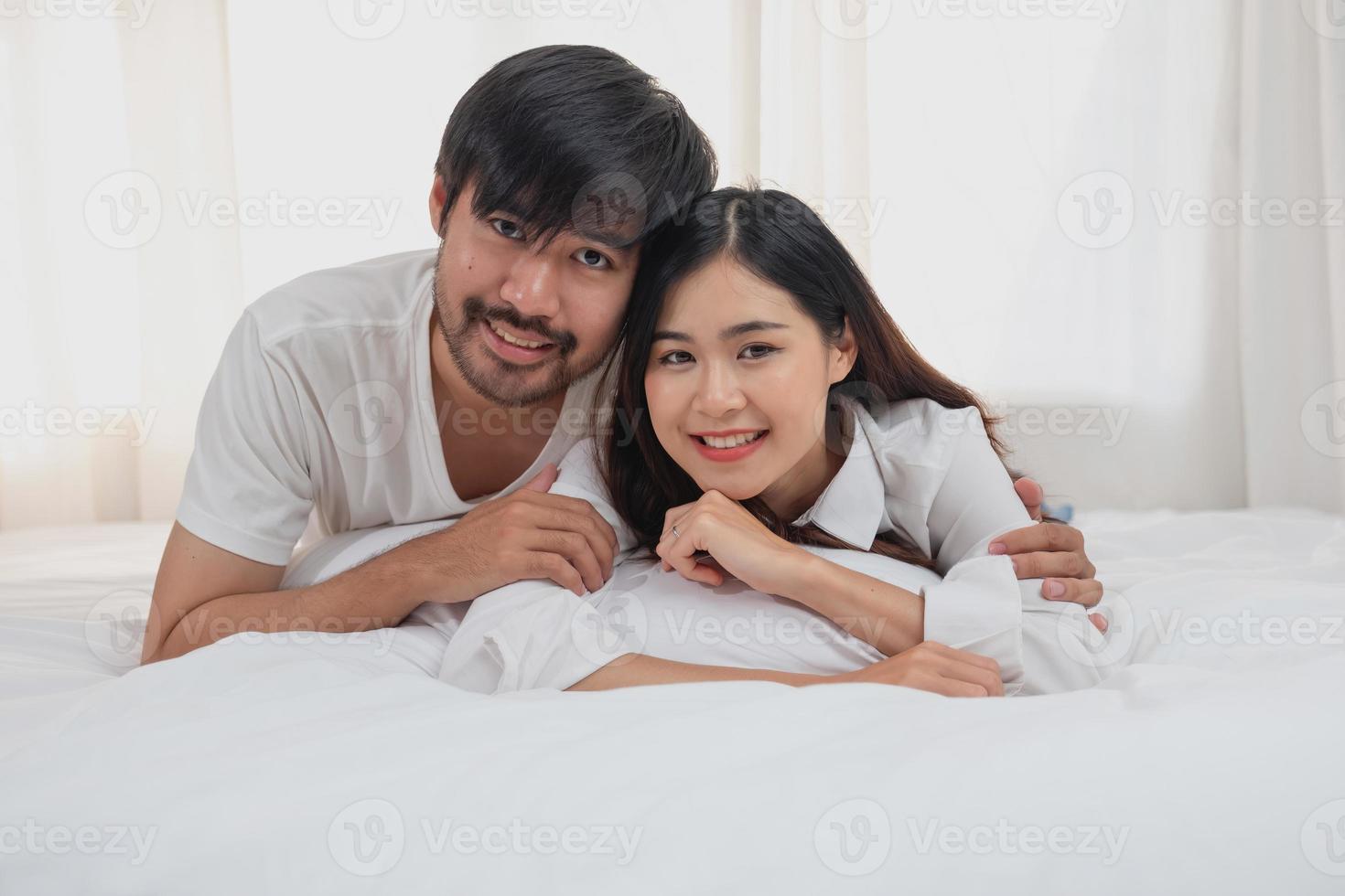 feliz jovem ásia casal abraçando, provocando, jogando alegremente dentro cama às lar, romântico Tempo para realçar família União. família conceito. foto