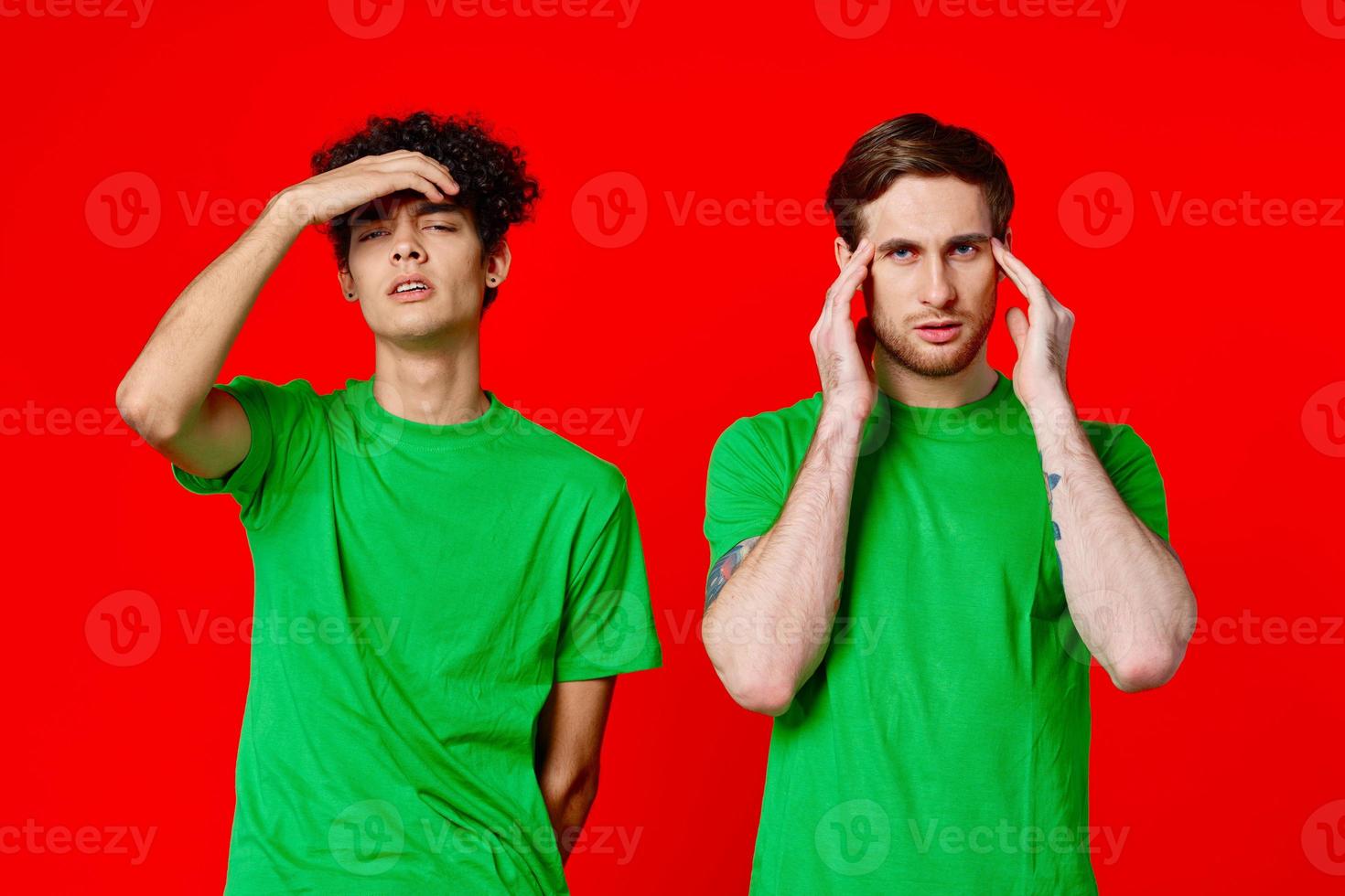 dois homens segurando seus cabeças dentro verde Camisetas em uma vermelho fundo foto