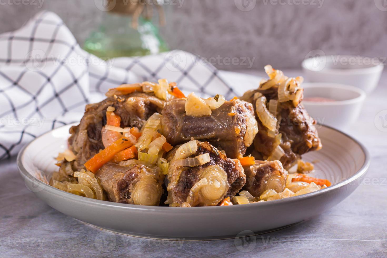 cozido rabo de boi com cenouras e cebolas em uma prato em a mesa foto