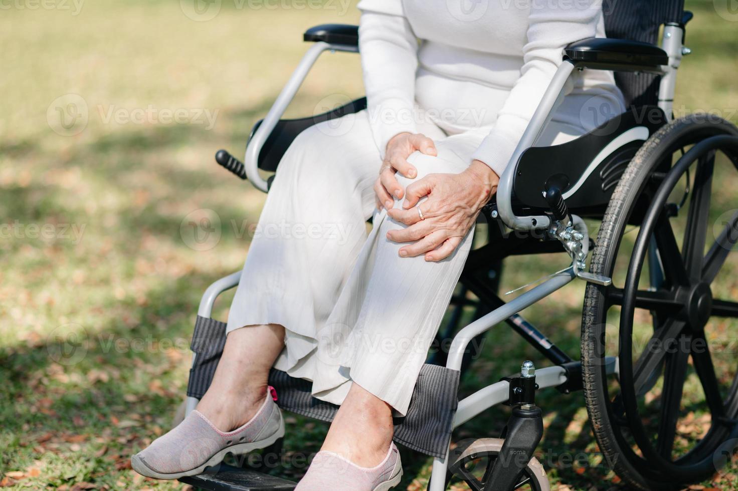 ásia velho mulher sentado em uma cadeira de rodas ao ar livre dentro a parque ter dor dentro a braços, pulsos e corpo dentro Sol luz foto