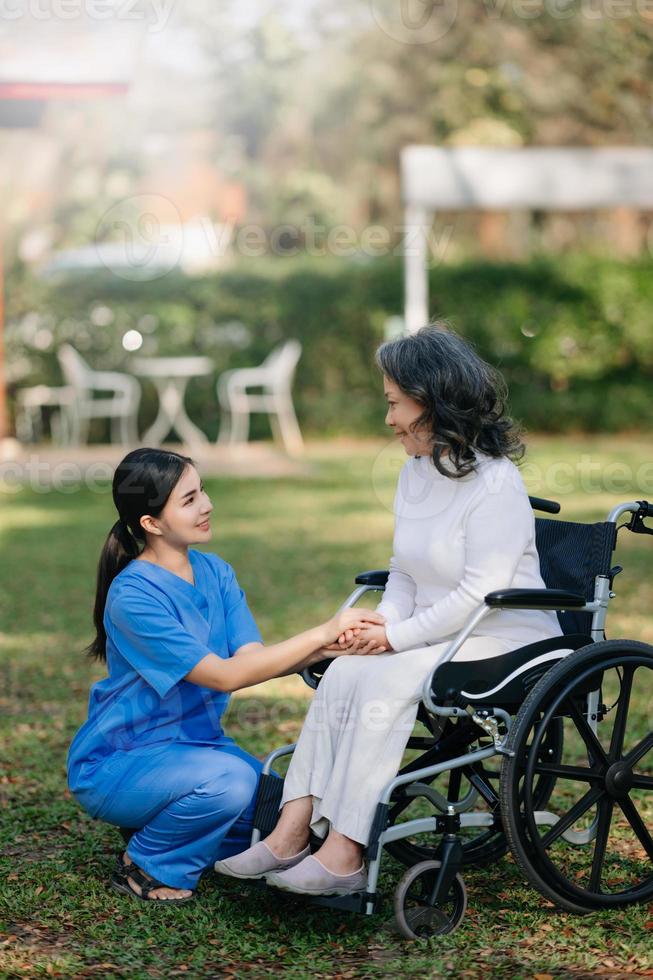 idosos ásia Senior mulher em cadeira de rodas com ásia Cuidado cuidador. enfermagem casa hospital jardim conceito. dentro Sol luz foto